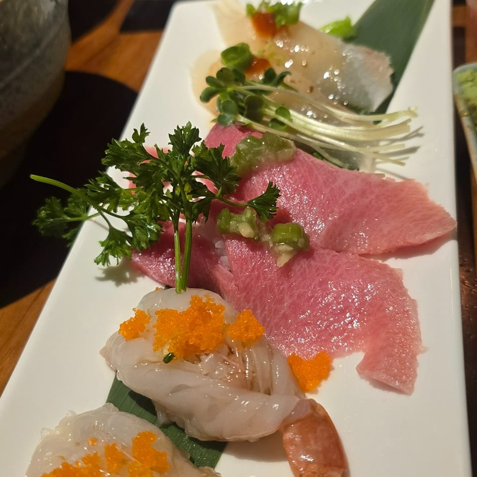Japanese sushi platter with shrimp topped with orange roe, fatty tuna, sashimi, garnishes, and sushi rolls on white plates.