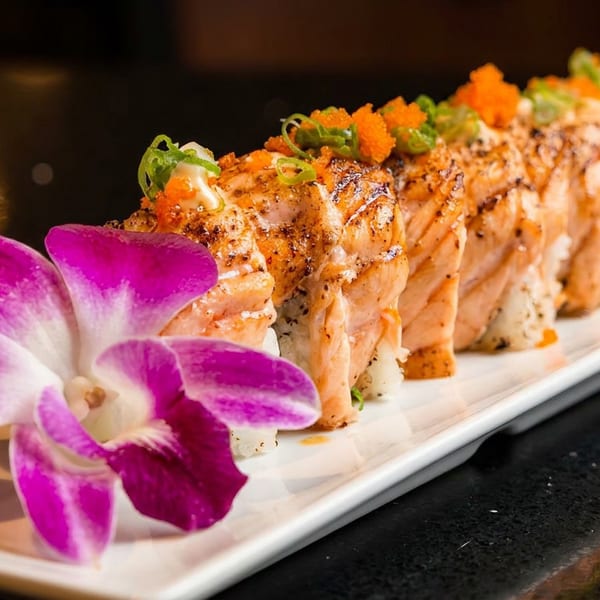 A plate of salmon sushi rolls garnished with roe, green onions, and a purple orchid.