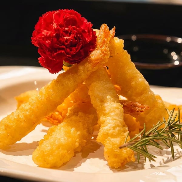 Crispy golden fried shrimp tempura, garnished with a red flower and rosemary sprig on a white plate.