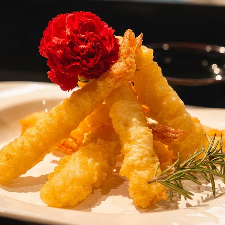 Crispy golden fried shrimp tempura, garnished with a red flower and rosemary sprig on a white plate.