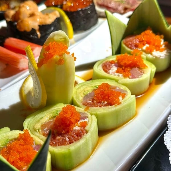 Plate of sushi rolls wrapped in cucumber and topped with orange fish roe, alongside seaweed-wrapped nigiri and garnishes.