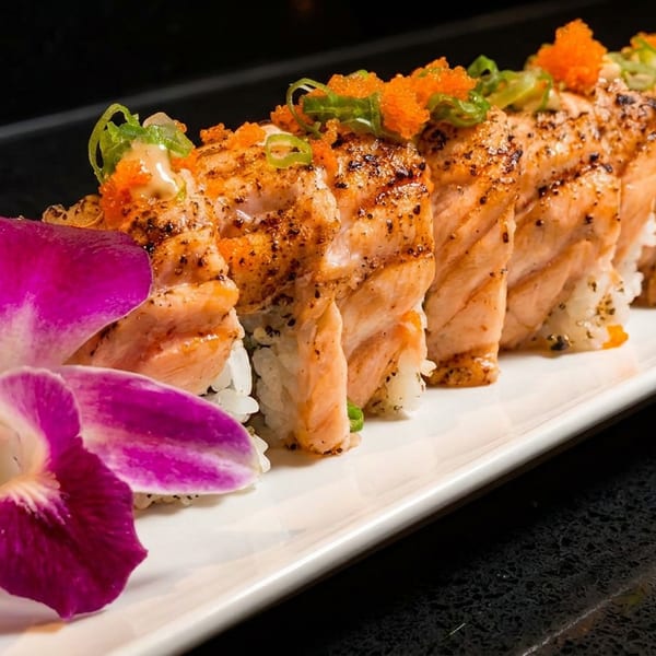 Seared salmon sushi rolls topped with roe and green onions, garnished with a purple orchid.