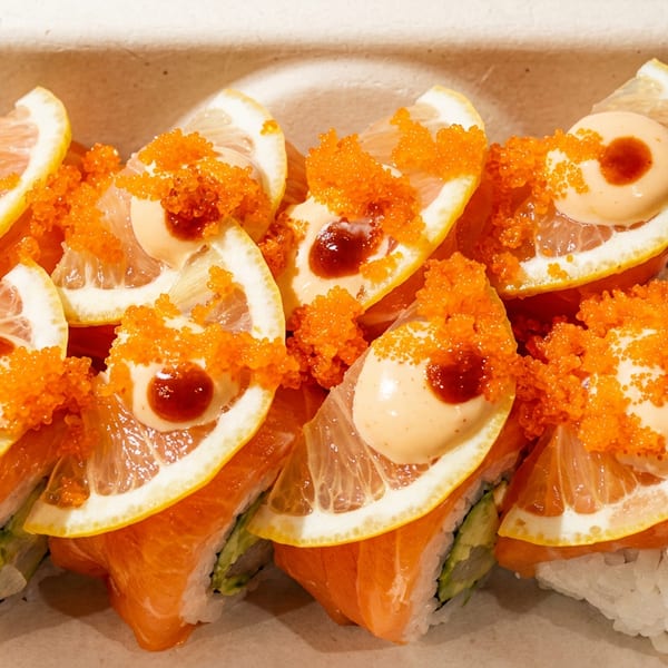 Salmon sushi rolls topped with lemon slices, orange tobiko, and creamy sauce, garnished with an orchid.