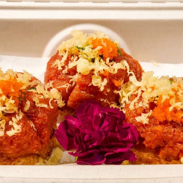 Three spicy tuna crispy rice appetizers topped with tempura flakes and roe, garnished with a purple flower.