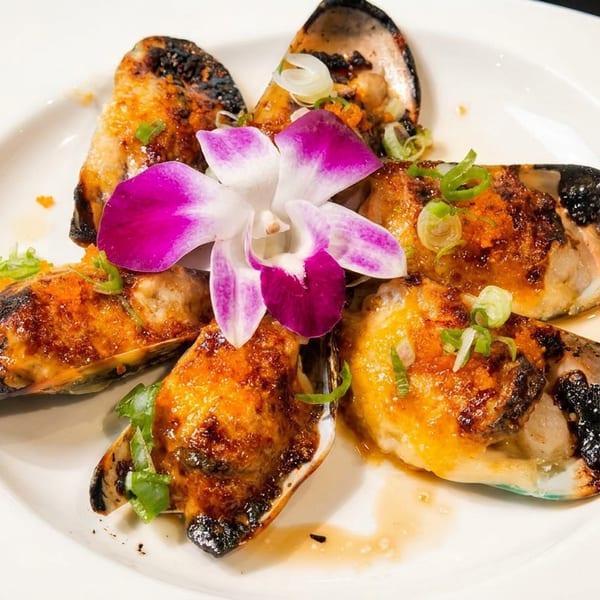 Grilled mussels topped with green onions and a purple orchid on a white plate.