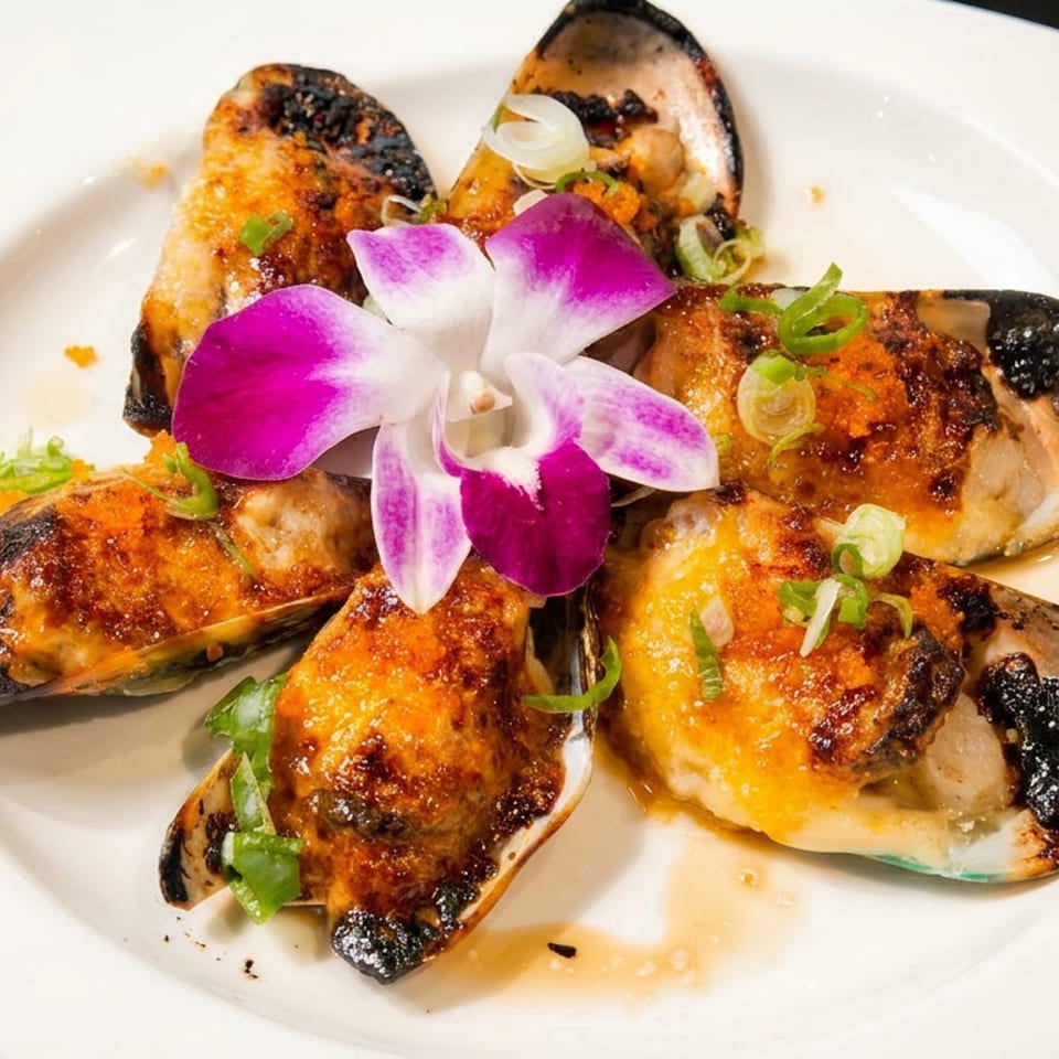 Grilled mussels topped with green onions and a purple orchid on a white plate.